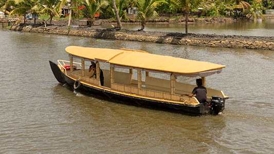 Shikkara houseboat gliding through calm Kochi backwaters surrounded by coconut trees and narrow canals.